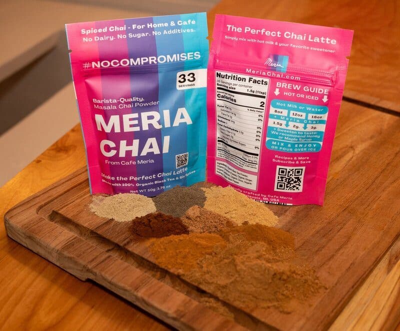 Two pouches of Meria Chai on a wood board with the six ground spices